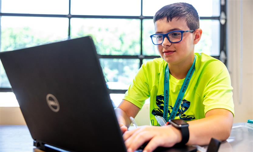 A boy wearing a yellow shirt uses a laptop